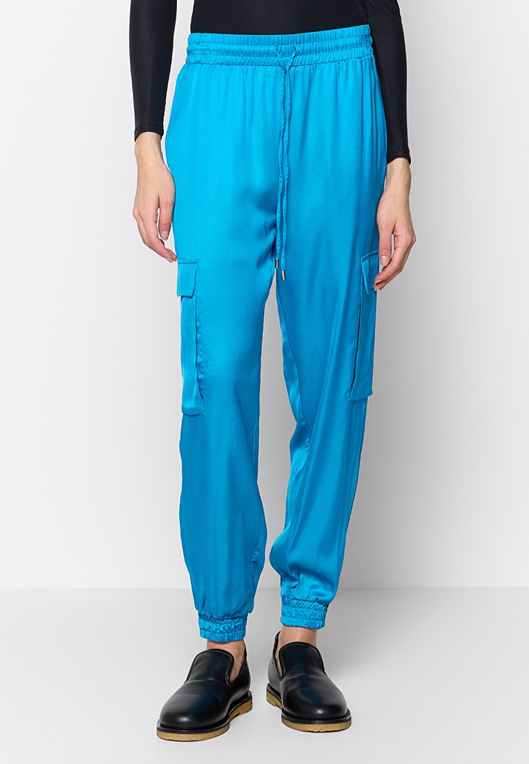 Pantalons jogger turquoise avec une taille élastique, cordon de serrage, deux poches latérales et poignets élastiques aux chevilles. Texture lisse.