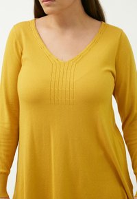 Maglioncino giallo a maglia con scollatura a V, caratterizzato da cuciture verticali testurizzate sul davanti e maniche lunghe. Tessuto morbido e leggero.