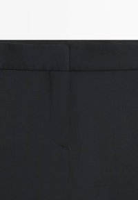 Close-up of the waist area of black trousers showing a hidden hook-and-bar fastening with a flat waistband.