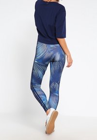 Granatowy crop top w połączeniu z dopasowanymi legginsami z wirującym niebieskim wzorem. Legginsy mają boczne paski i gładką, elastyczną teksturę.