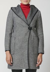 Cappotto a motivo pied-de-poule in bianco e nero con un colletto grigio oversize, rifiniture nere e tasche frontali, chiuso con un bottone in vita.