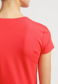 Kortärmad t-shirt i livlig korall, tillverkad av mjuk, stretchig tyg. Har en rundad halsringning och jämn textur.