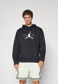 Sort hættetrøje med kengurulomme, præget af en hvid Jumpman-logo og "23" grafik. Båret med lyse shorts.