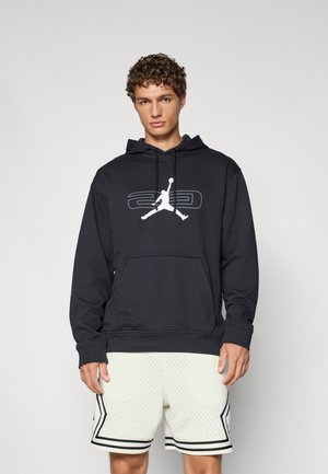 Sort hættetrøje med kengurulomme, præget af en hvid Jumpman-logo og "23" grafik. Båret med lyse shorts.
