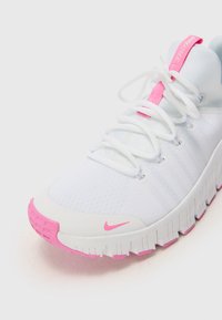 Hvide atletiske sko med en struktureret overdel og pink detaljer. Har en rund tå, snørebånd og en tyk hvid sål med pink accentuer.