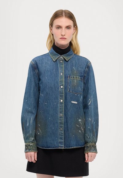 Cămașă din denim de culoare albastru deschis, cu guler clasic, închidere cu nasturi pe față, buzunar pe pieptul stâng și detalii de stropi de vopsea pe mâneci.