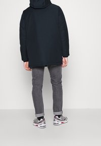 Černá károvaná bunda s volnějším střihem, doplněná šedými denimovými kalhotami. Obuv má sportovní design v šedé, bílé a červené.