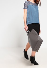 Lyseblå satinbluse med blondekortærmer, parret med en sort nederdel og en grå totebag. Sorte ankelstøvler fuldender looket.