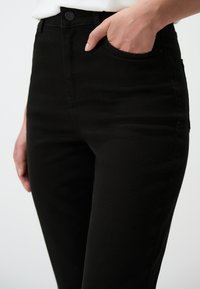 Czarne dżinsy wąskie, wyposażone w przednie kieszenie oraz zapięcie na guzik. Tkanina ma gładką fakturę i lekki stretch.