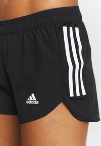 Mustat urheilushortsit, jotka on valmistettu sileästä kankaasta. Shortsseissa on valkoinen Adidas-logo ja kolme pystysuoraa raitaa sivuilla, sekä halkiopääntie.