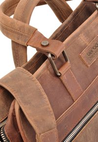 Bruine leren tas met een ritsluiting, stevige draaghandvatten en zichtbare stikseldetails; het ontwerp benadrukt duurzaamheid en functionaliteit.