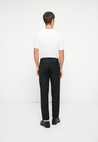 Schwarze Hosen mit maßgeschneidertem Schnitt, die einen glatten Stoff, einen elastischen Bund und zwei Gesäßtaschen aufweisen, kombiniert mit einem schlichten weißen T-Shirt.