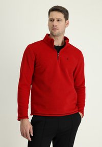 Pullover in fleece rosso con colletto a mezza zip, maniche lunghe e dettagli in stitching nero. Presenta un piccolo logo nero sul petto.