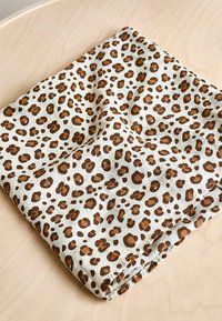 Leopárdmintás szövet szalvéta bézs háttérrel és barna foltokkal, texturált felülettel és varrott szélekkel, fa felületen pihen.