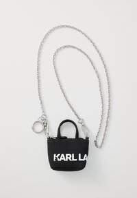 Mini sac en tissu noir avec chaîne en argent, équipé d'une poignée supérieure, d'une fermeture éclair et d'un grand logo blanc sur le devant.