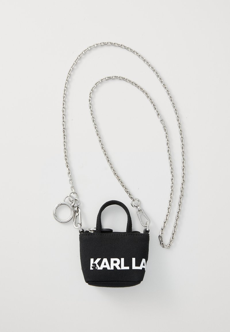 Mini sac en tissu noir avec chaîne en argent, équipé d'une poignée supérieure, d'une fermeture éclair et d'un grand logo blanc sur le devant.