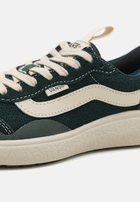 Žalios suede sportbačiai su grietinėlės akcentais, perforuotomis detalėmis ir tekstūruota guma. Yra klasikinis Vans logotipas ir plokščios raišteliai.