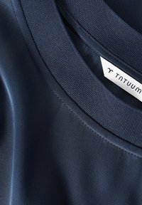 Navyblaues Stoff-T-Shirt mit glatter Textur und geripptem Rundhalsausschnitt. Etikett sichtbar mit "TNTUUM"-Markierung.