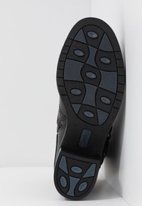 Black shoe sole with textured grip, featuring blue accents and oval treads for traction. Material appears rubber with a sleek design.