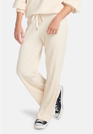 Pantaloni lounge a coste, color crema, con vita elasticizzata e cordoncino. Abbinati a sneakers in tela nere con suole bianche.