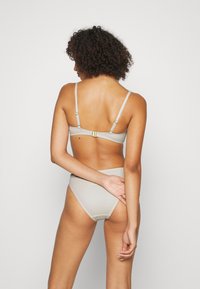 Conjunto de bikini cinza claro com um tecido texturizado, alças ajustáveis e um fecho de metal dourado nas costas do sutiã. Parte de baixo de cintura alta.