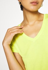T-shirt a V in un vivace giallo neon, realizzata in tessuto morbido, con maniche corte e una forma aderente che mette in risalto il collo e le spalle.