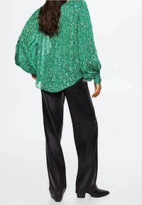 Blouse verte à motif avec manches bouffantes, associée à un pantalon en cuir noir taille haute et des bottines à talons.