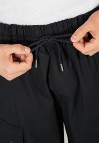 Schwarze Hose mit elastischem Bund und Zugkordel. Der Stoff wirkt leicht und hat eine strukturierte Oberfläche, mit vorderen Taschen.