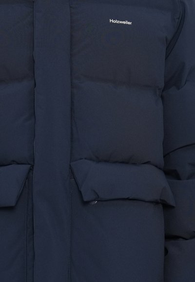 Navy plavi jakna od jastučića s kvadratnom teksturom, s visokim ovratnikom, bočnim džepovima i logotipom na gornjoj lijevoj strani.