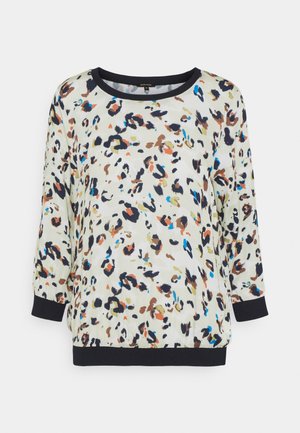 Blusa blanca de manga larga con un estampado abstracto de leopardo multicolor y ribete negro en el escote, los puños y el dobladillo.