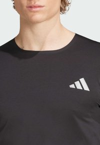Zwarte T-shirt met korte mouwen van ribstof, met een reflecterende drie-strepen logo-accent aan de linkerkant van de borst.