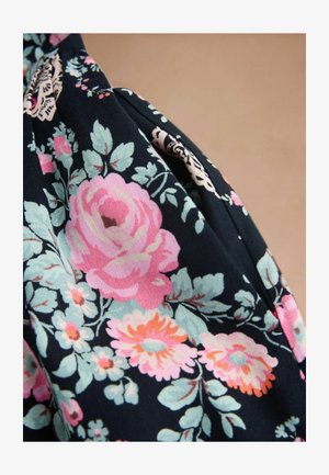 Tela oscura con un patrón floral que presenta grandes flores rosas, naranjas y azul claro, junto con hojas verdes sobre un fondo beige.