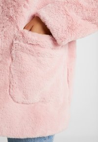 Pinkfarbener Kunstpelz mit weicher Textur, vorne mit Tasche und lockerem Schnitt, passend zu lässigem Denim.