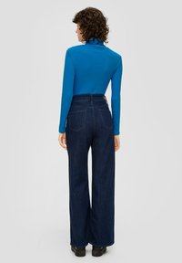 Strakke blauwe top met lange mouwen, gecombineerd met hoge taille, wijde denimmutsen in een donkere kleur. Heeft vier achterzakken en een gladde stoftextuur.
