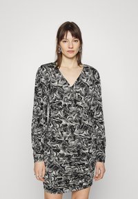 Vestido com padrão em preto e branco, com mangas longas, decote em V e textura franzida na cintura, apresentando um design em espiral por toda a peça.