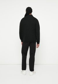 Maglione lavorato a maglia nero con una vestibilità morbida, collo rotondo e polsini a coste. Abbinato a pantaloni cargo neri e sneakers bianche. Sfondo semplice.