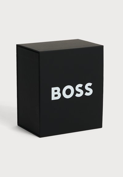 Boîte rectangulaire noire avec le mot "BOSS" en grandes lettres blanches sur le devant, affichée sur un fond blanc uni.