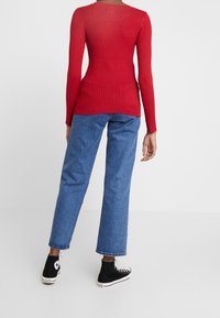 Maglietta rossa a coste con maniche lunghe abbinata a jeans blu a gamba dritta e sneakers nere alte. La maglietta presenta un collo rotondo e un design aderente.