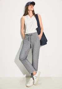 Grå joggerbyxor med elastisk midja och dragsko, kombinerat med en vit ärmlös topp och vita sneakers med ljusa accenter.