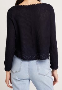 Maglione lavorato a maglia blu navy con un motivo testurizzato, maniche a tre quarti e scollatura ondulata; presenta un design decorativo all'orlo.