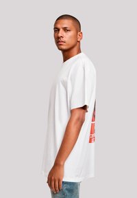 Weißes Baumwoll-T-Shirt mit kurzen Ärmeln, das auf der Rückseite ein buntes grafisches Design zeigt. Die Passform ist lässig und leicht übergroß.