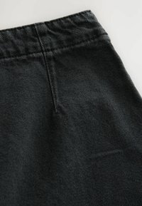 Black denim fabric showcasing a close-up of a waistband with textured weave and vertical seam detailing. Soft, matte finish.