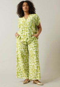 Groene bloempatronen blouse en wijde broek van lichtgewicht stof; heeft een relaxte pasvorm, korte mouwen en zijzakken. Gouden flats.