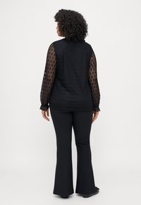 Μαύρο πουκάμισο με μακρυά μανίκια από μοτίβο δαντέλας, διαθέτοντας στρογγυλή λαιμόκοψη και μαζεμένες μανσέτες. Συνδυάζεται με μαύρες φαρδιές παντελόνες.