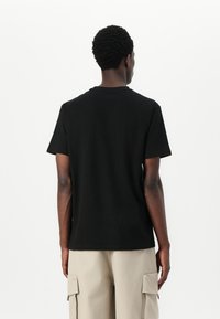 Black cotton t-shirt with short sleeves, crew neck, and a relaxed fit, viewed from the back. Paired with light beige cargo shorts.