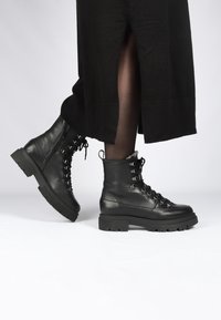 Zwarte leren enkellaarsjes met een dikke zool, veters aan de voorkant en metalen accenten. Voorzien van een gevoerde kraag en een gestructureerd bovenwerk.