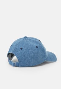 Gorra de béisbol de denim en azul claro con ala curvada, correa ajustable y ojales para ventilación. Presenta un detalle bordado en la parte superior.