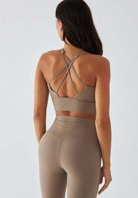 Brązowy sportowy biustonosz z krzyżującymi się paskami z tyłu, w połączeniu z dopasowanymi legginsami z wysokim stanem w tym samym kolorze.
