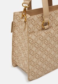 Beżowa torebka z fakturowanym wykończeniem i wzorzystym designem, z elementami w złotym kolorze oraz podwójnymi uchwytami. Ustrukturyzowany prostokątny kształt.