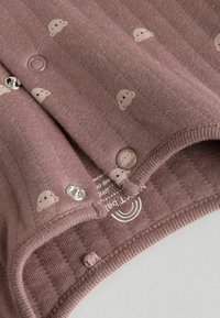 Afdæmpet mauve bomuldsheldragt med teksturerede striber; har små skymønstre, metalsnapper og en rund knap med et tegneserieansigt.